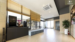 Un hall d’hôtel moderne avec un comptoir d’accueil, un espace salon et de grandes fenêtres.