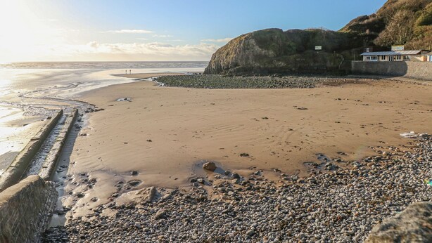 A coastal beach with a rocky shoreline, a building on the right, and a clear sky. - Little Brook Cottage (Carmarthen)