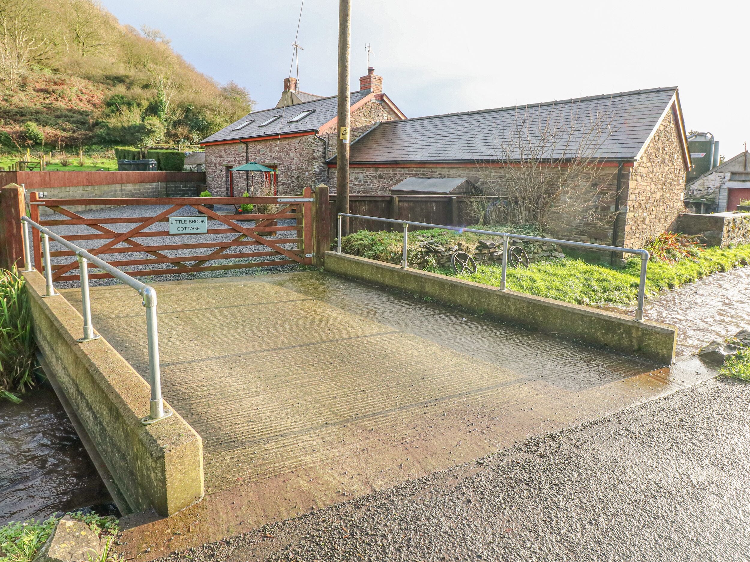 A gated entrance to a property with a stone building, a metal gate, and a gravel path leading to a water feature.