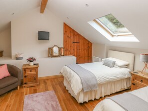 A bedroom with a sloped ceiling, wooden wardrobe, a bed with white bedding, a small bedside table, a lamp, and a skylight. - Little Brook Cottage (Carmarthen)