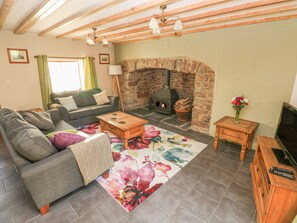 A cozy living room with a stone fireplace, a sofa set, a coffee table, and a TV stand. - Little Brook Cottage (Carmarthen)