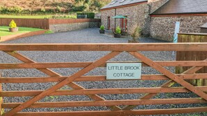 A cottage with a stone exterior, a gravel driveway, and a wooden gate with a sign reading "Little Brook Cottage". - Little Brook Cottage (Carmarthen)