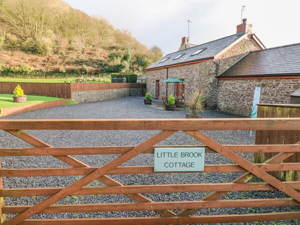 A cottage with a stone exterior, a gravel driveway, and a wooden gate with a sign reading "Little Brook Cottage". - Little Brook Cottage (Carmarthen)