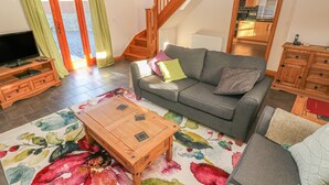 A living room with a sofa, coffee table, and a TV on a wooden stand. - Little Brook Cottage (Carmarthen)