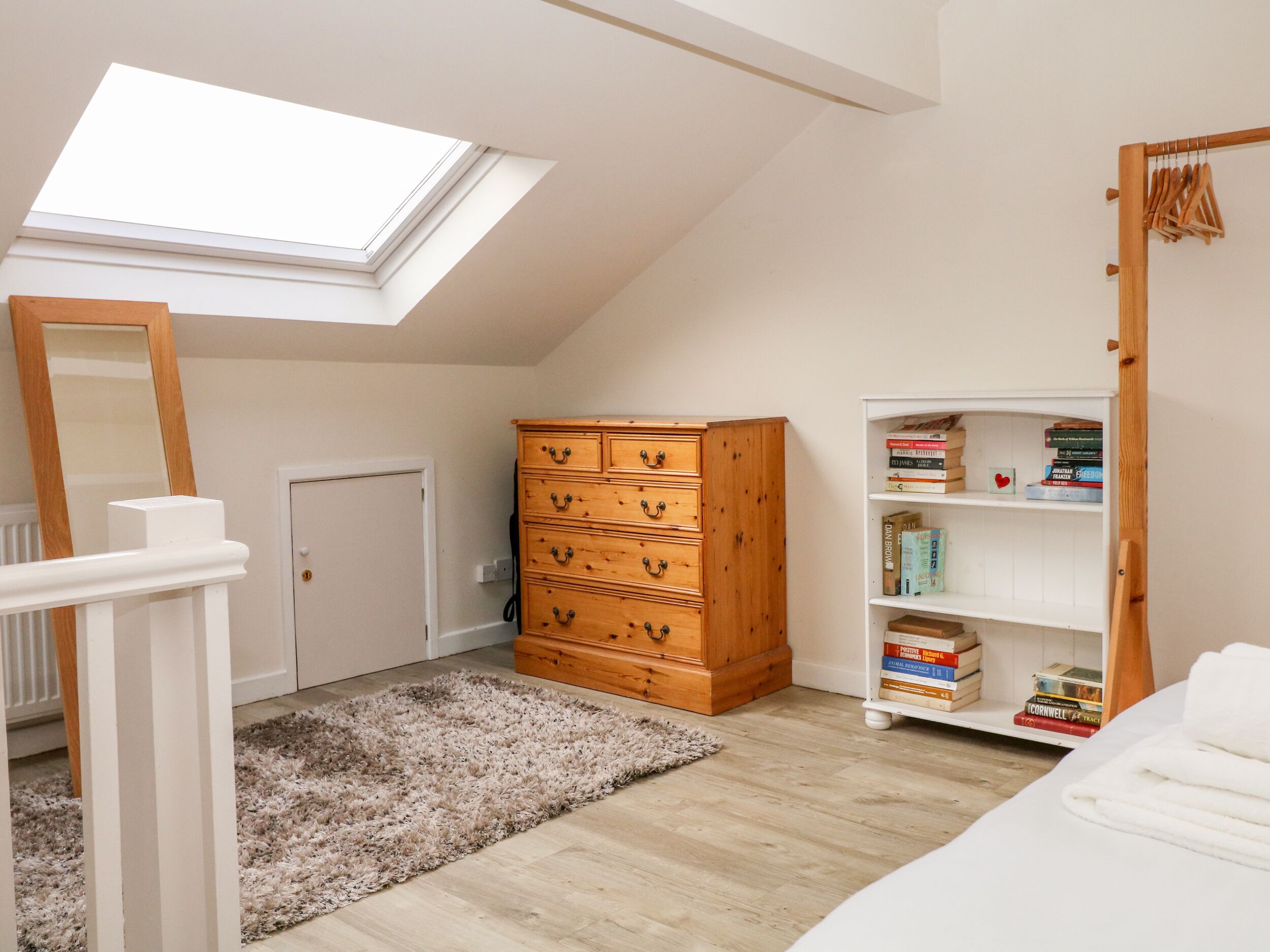 A room with a skylight, wooden dresser, bookshelf, and a white door.