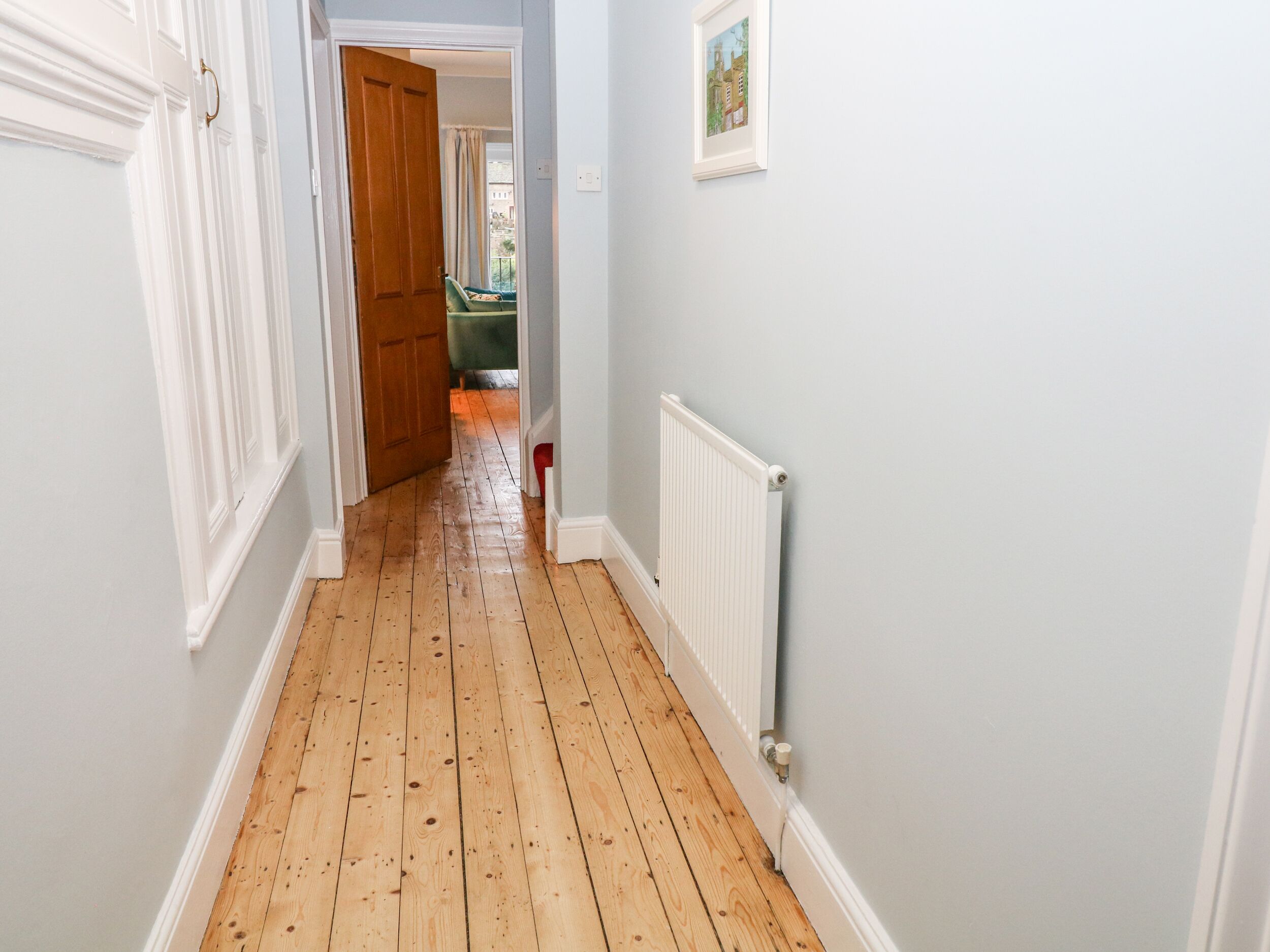 A hallway with wooden flooring, white walls, and a radiator.