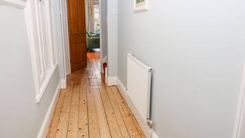 A hallway with wooden flooring, white walls, and a radiator.