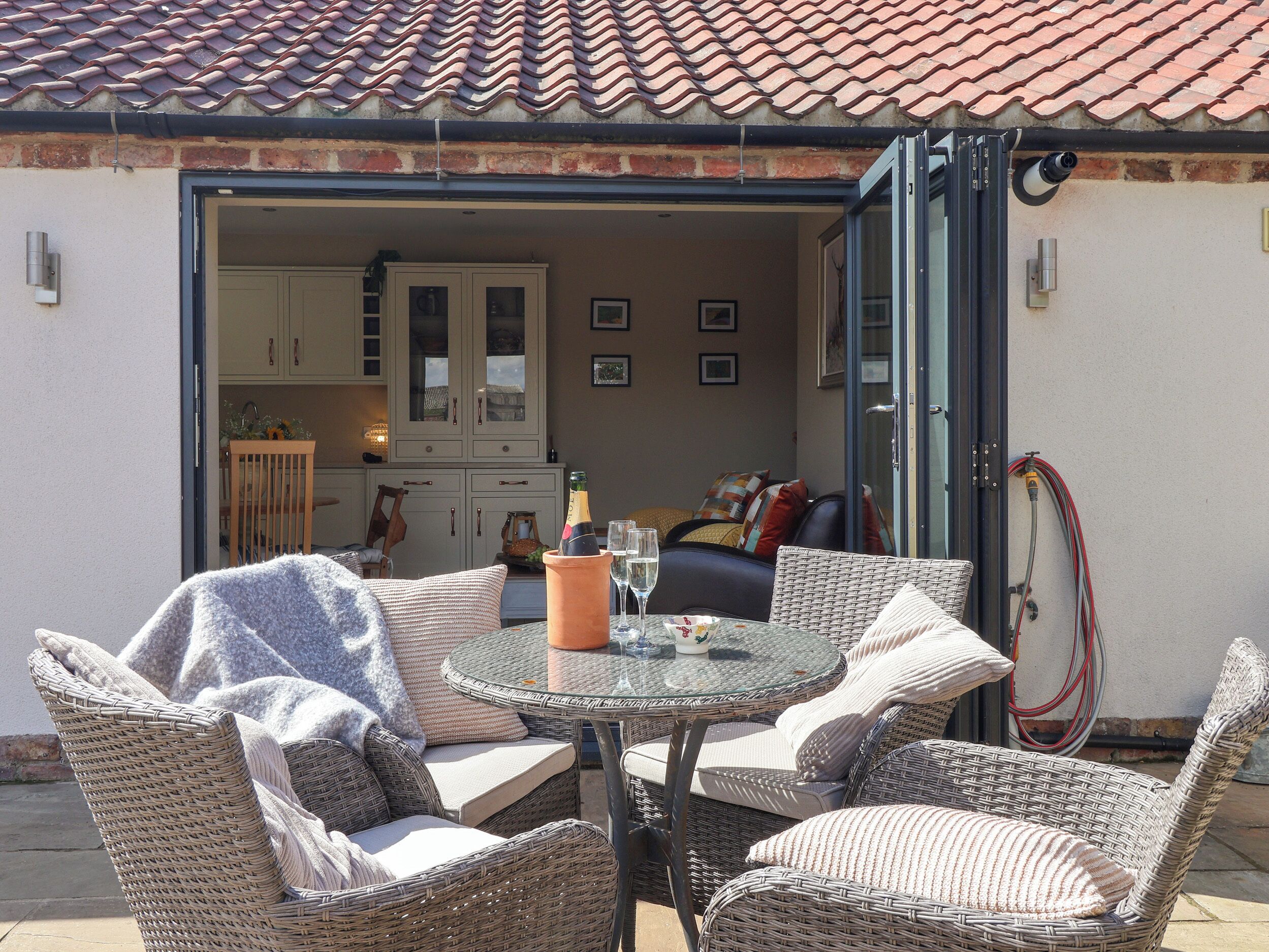 Eine offene Terrasse mit Korbmöbeln, einem Glastisch und Blick in eine Küche mit Schränken und einem Essbereich.