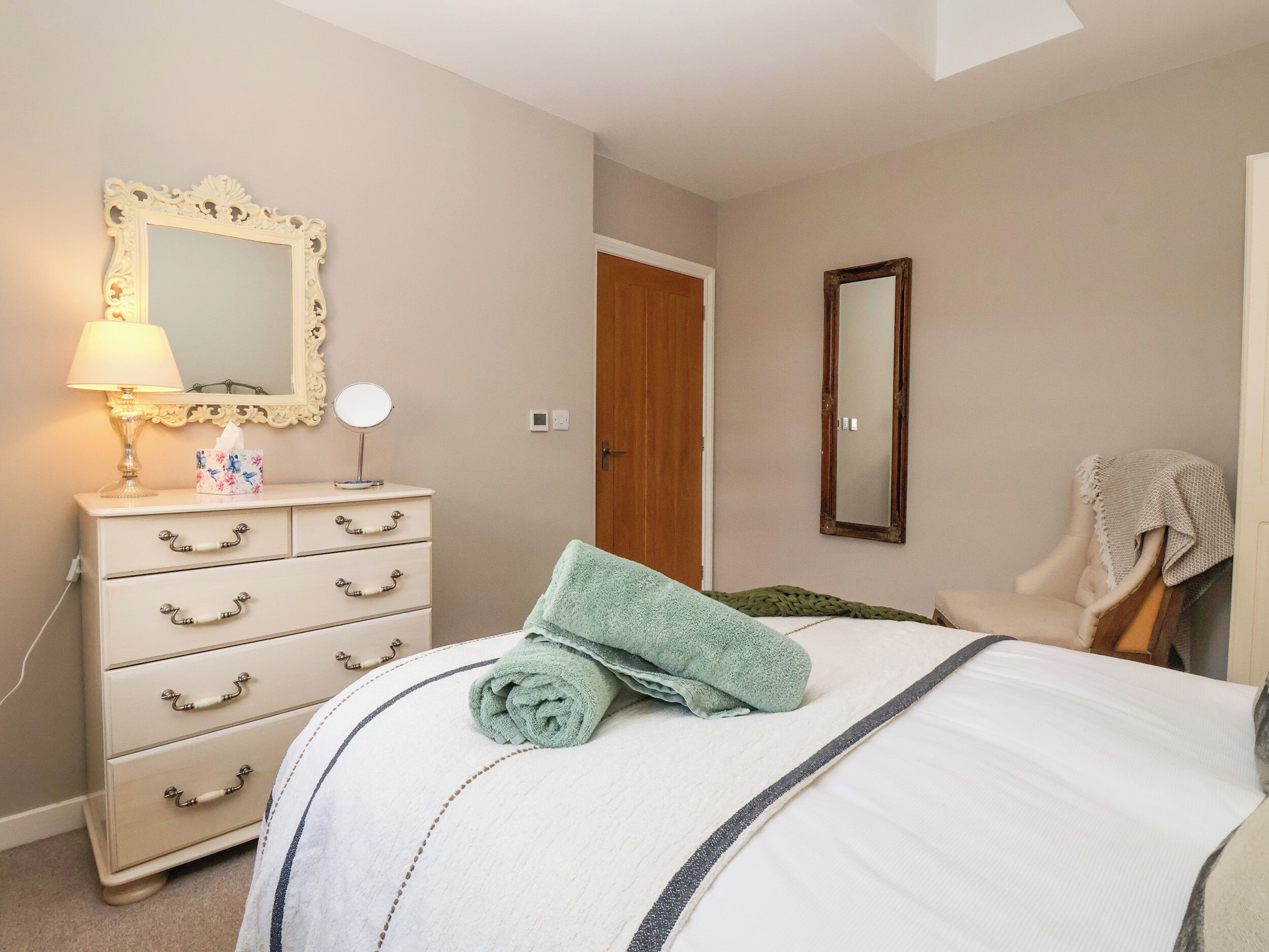 A bedroom with a bed, a dresser with drawers, a mirror, a lamp, and a door.