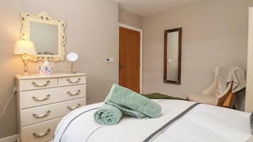 A bedroom with a bed, a dresser with drawers, a mirror, a lamp, and a door.