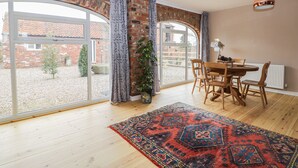 A spacious room with a large window, a dining table with chairs, and a patterned rug. - Pipistrelle Cottage (Beverley)