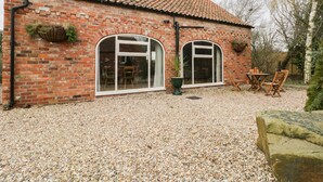 A brick house with two large arched windows, a tiled roof, and a gravel driveway. - Pipistrelle Cottage (Beverley)