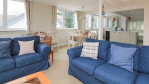A spacious living area with two blue sofas, a dining table, and a kitchen area with white cabinets and copper pendant lights. - Lanapoule (Salcombe)