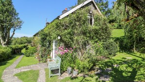 Ein charmantes Haus mit einem Steinweg, der zu einer hölzernen Bank führt, umgeben von üppiger Bepflanzung und blühenden Blumen.