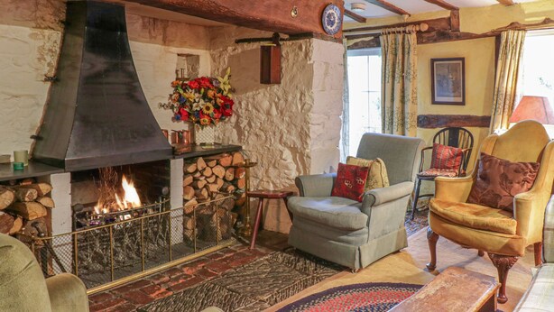 Ein gemütliches Wohnzimmer mit Kamin, Holzbalken, einer Steinwand und bequemen Sitzmöglichkeiten.