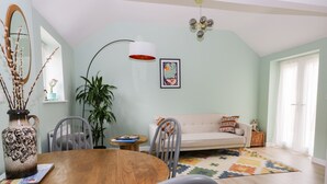 Un salon spacieux avec une table à manger en bois, des chaises grises, un canapé beige et un tapis coloré.