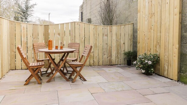 Une terrasse avec une table et des chaises en bois, une plante en pot et un sol carrelé en pierre.