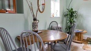 Un coin repas avec une table ronde en bois, des chaises grises, un vase avec des branches, un miroir et une plante en pot.