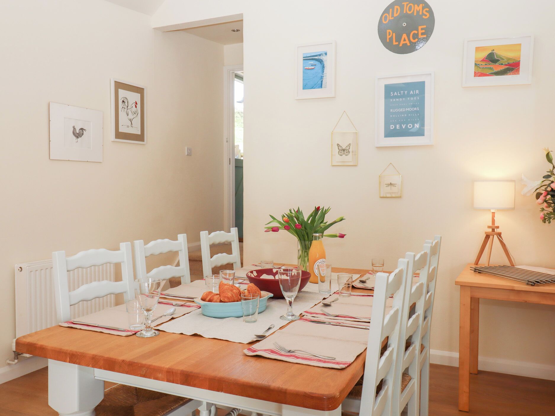 A dining area with a wooden table set for four, white chairs, and a vase with flowers.