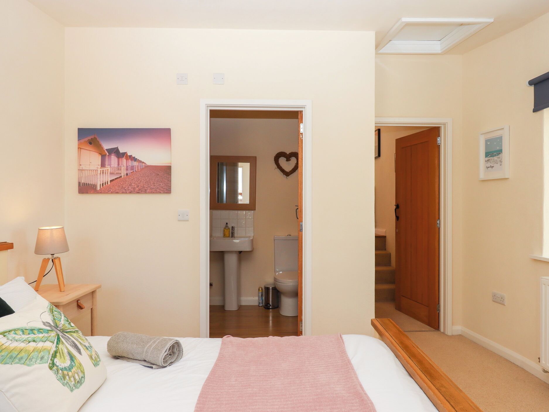 Een slaapkamer met een bed, een bedlamp, een schilderij en een zichtbare badkamer door een open deur.