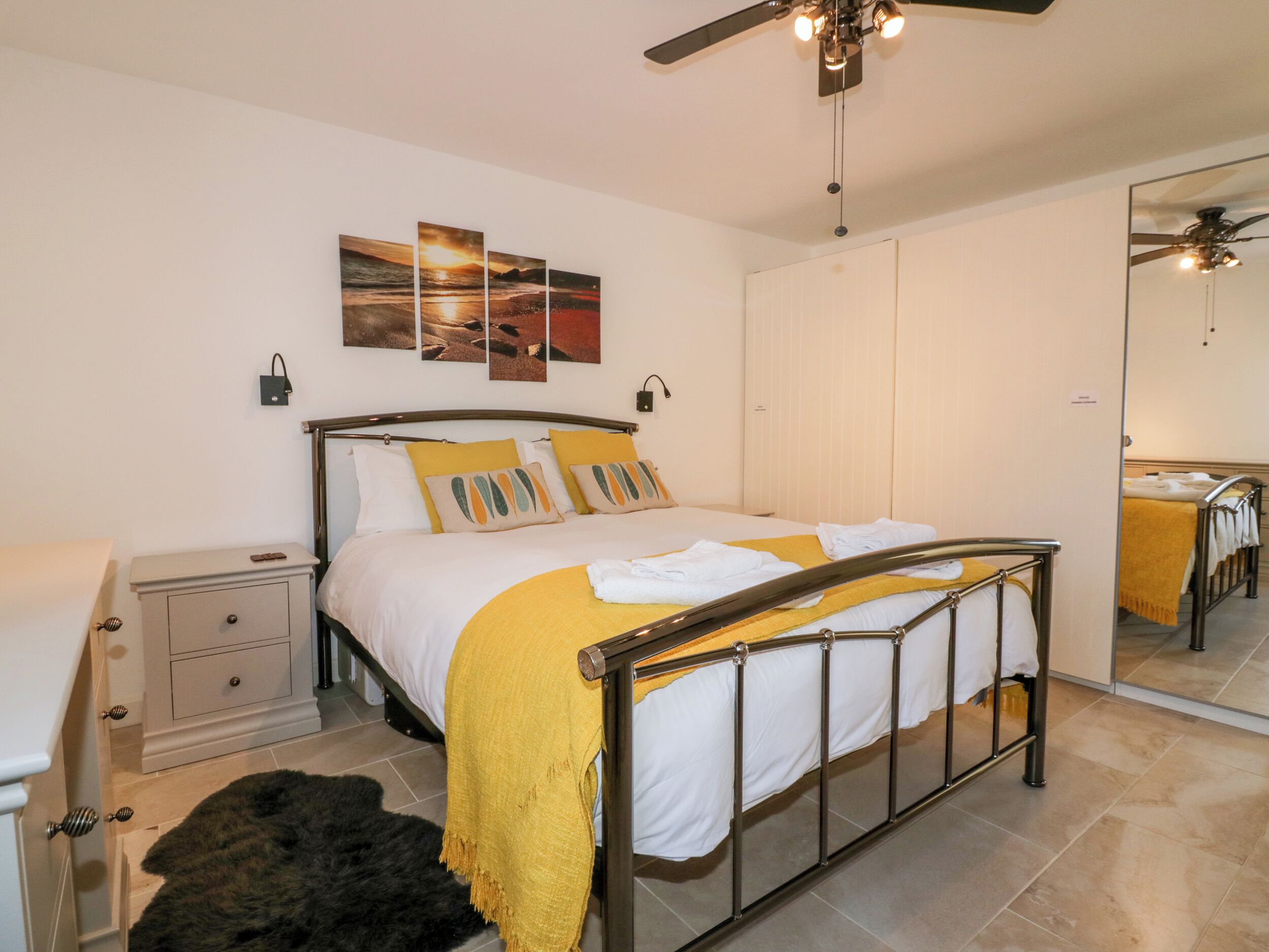 A bedroom with a bed, a nightstand, a mirror, and a ceiling fan.