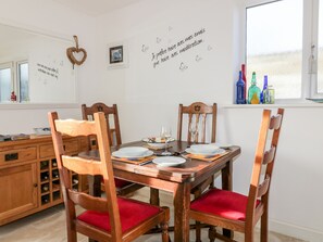 A dining room with a wooden table set for four, red cushioned chairs, a wall with decorative text and butterflies, and a window with bottles on the sill. - 3 Spyrys Heyl (Newquay)