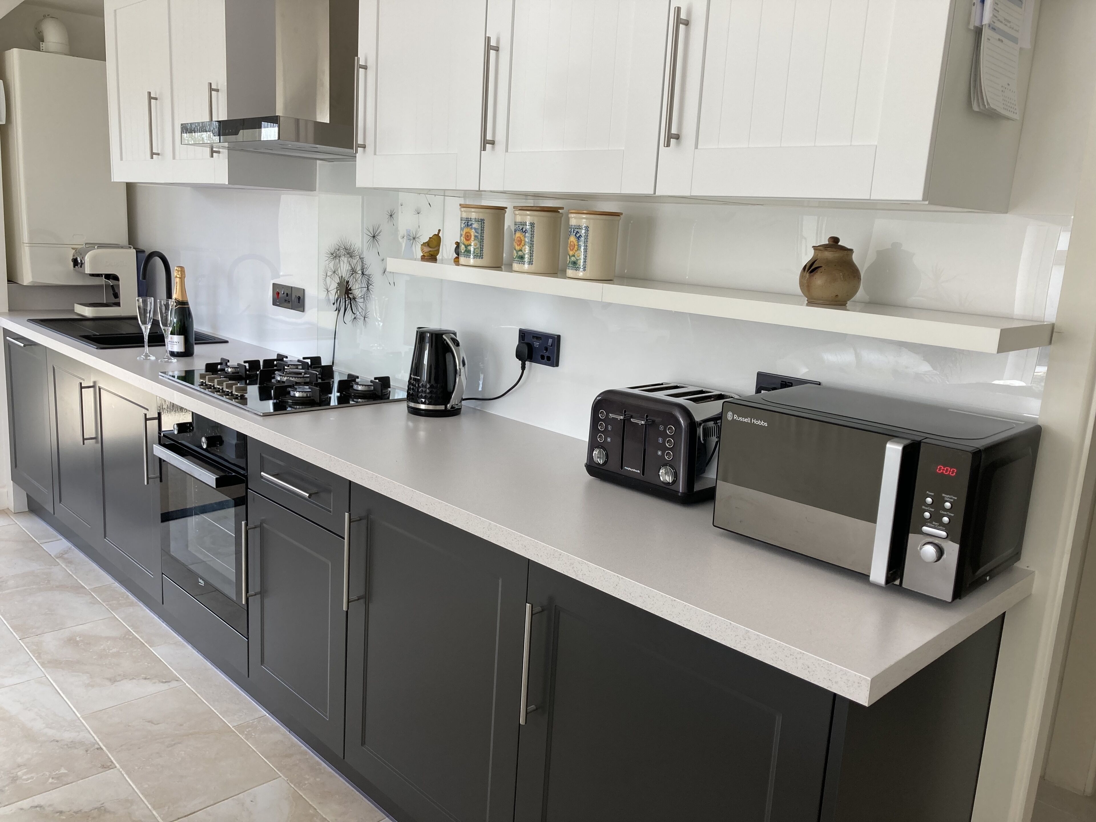 A modern kitchen with a built-in oven, a toaster, a kettle, and a microwave.