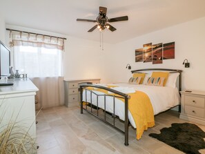 A bedroom with a bed, bedside tables, a ceiling fan, artwork on the wall, and a window with curtains. - 3 Spyrys Heyl (Newquay)