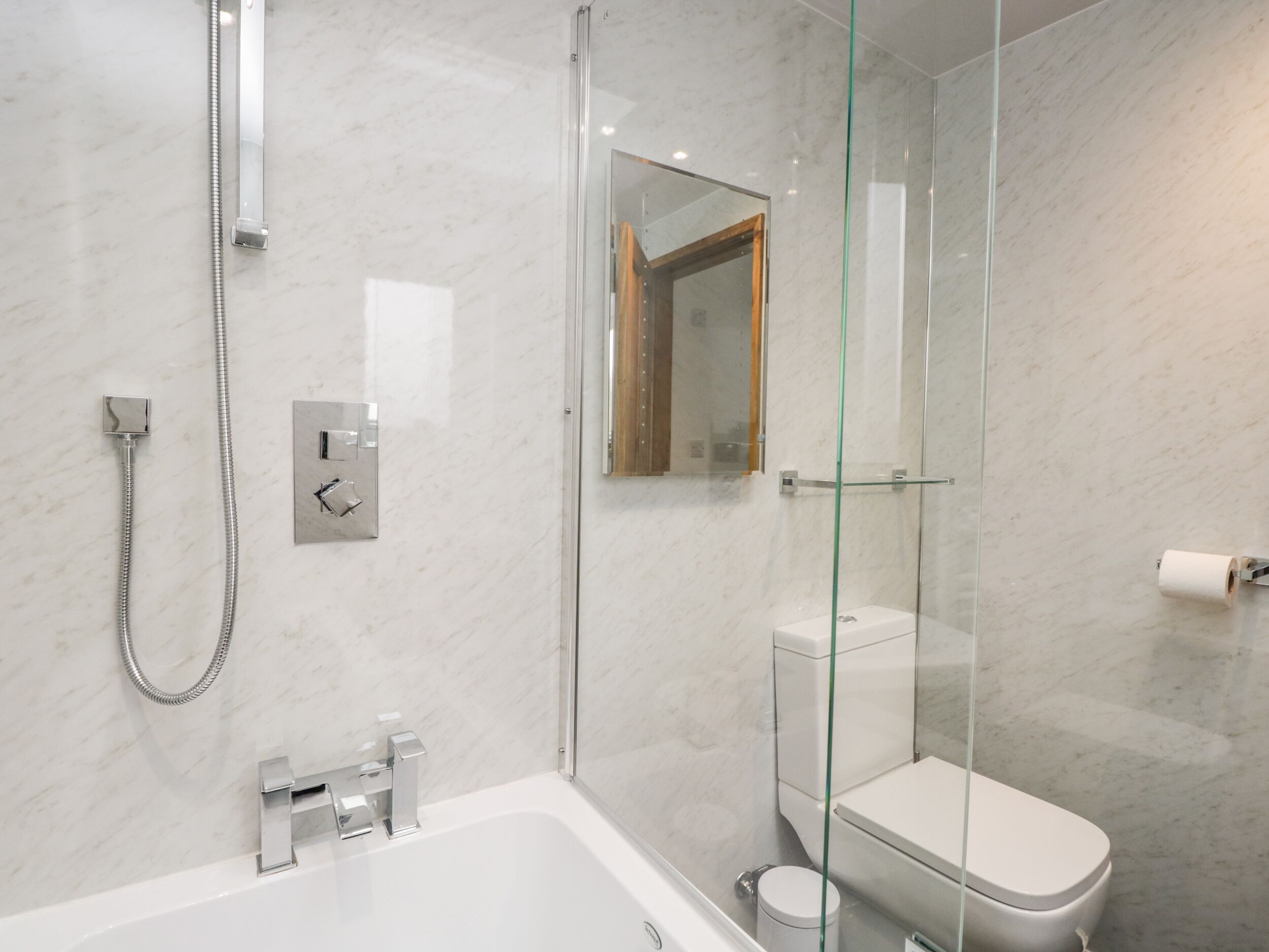 A modern bathroom with a glass-enclosed shower, a white bathtub, and a toilet.