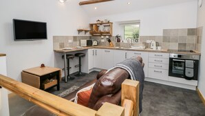 Une cuisine moderne équipée d’un four encastré, d’un four à micro-ondes et d’un évier. On y trouve une table à manger en bois et deux tabourets de bar. Un téléviseur est fixé au mur, au-dessus du plan de travail de la cuisine.