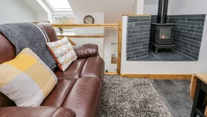 Un salon chaleureux avec un canapé en cuir marron, un plaid à motifs et un tapis noir et blanc. Un poêle à bois noir est encastré dans un mur dont la façade est en pierre.