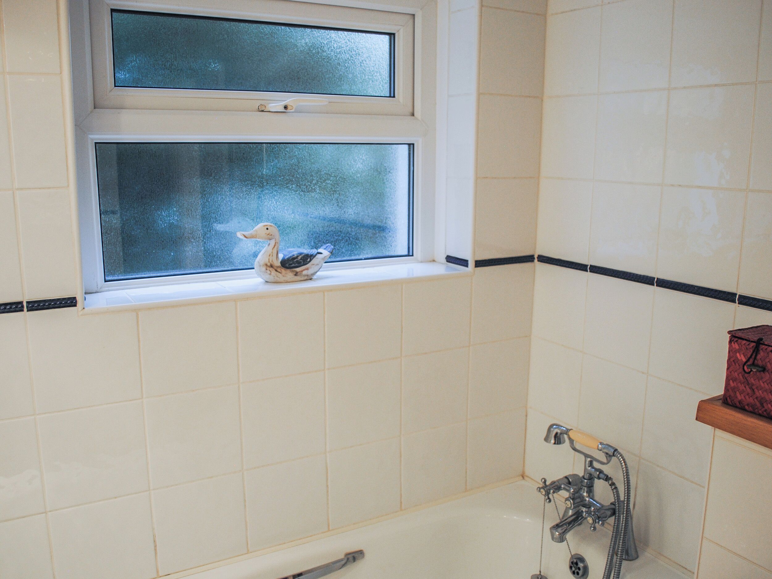 Een badkamer met een badkuip, een raam met een decoratieve eend, en een handdoekhouder.