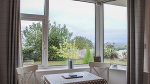 A room with a table and chairs by a large window overlooking a garden. - Fairview (Salcombe)
