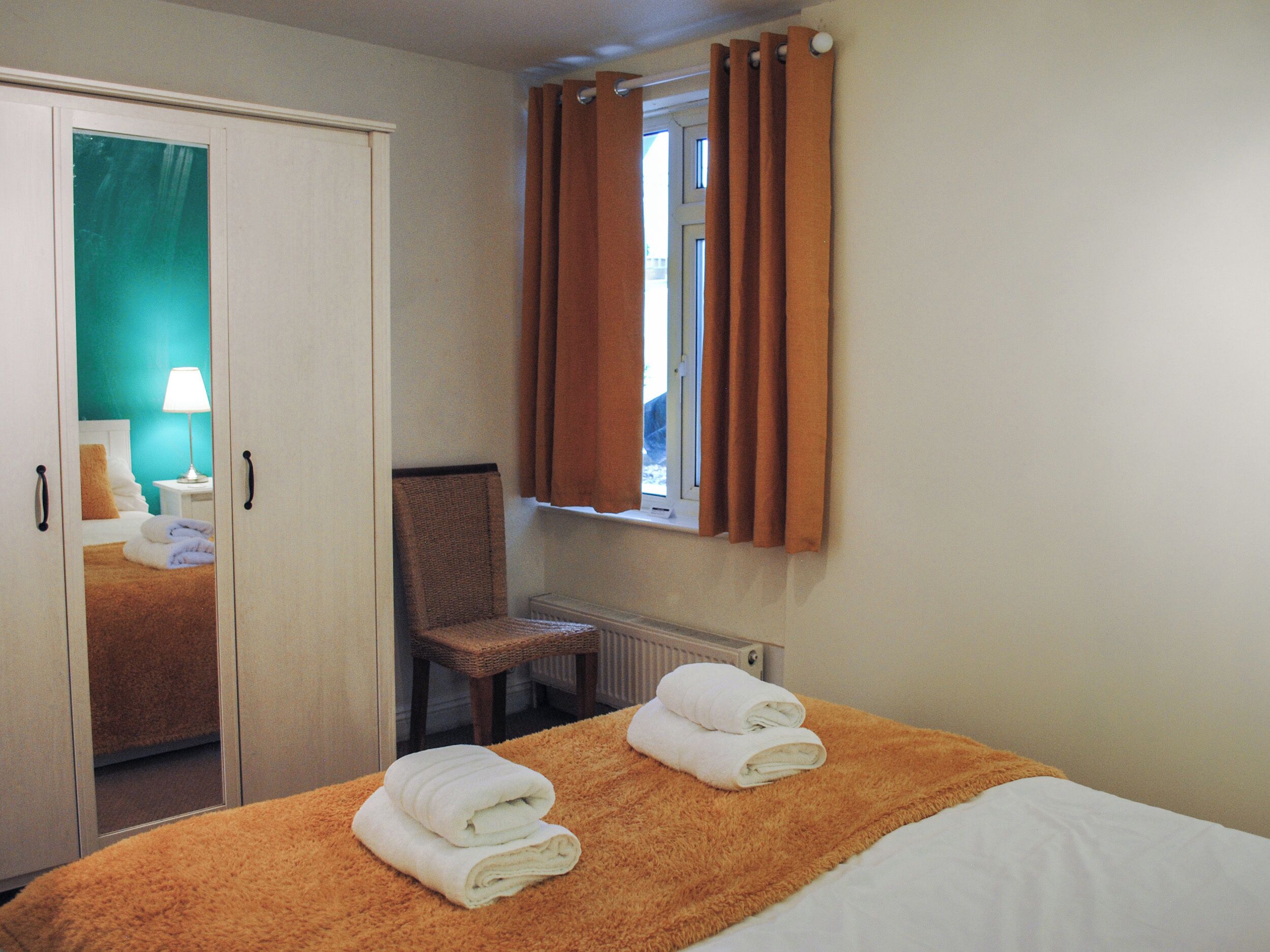 A hotel room with a bed, a chair, a window with curtains, a radiator, and a door leading to another room.