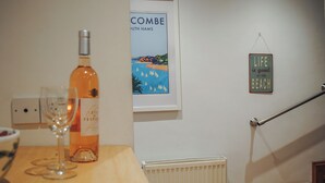 A room with a wooden table, a bottle of wine, a glass, a framed picture of a beach, and a sign saying "Life is good at the beach". - Fairview (Salcombe)