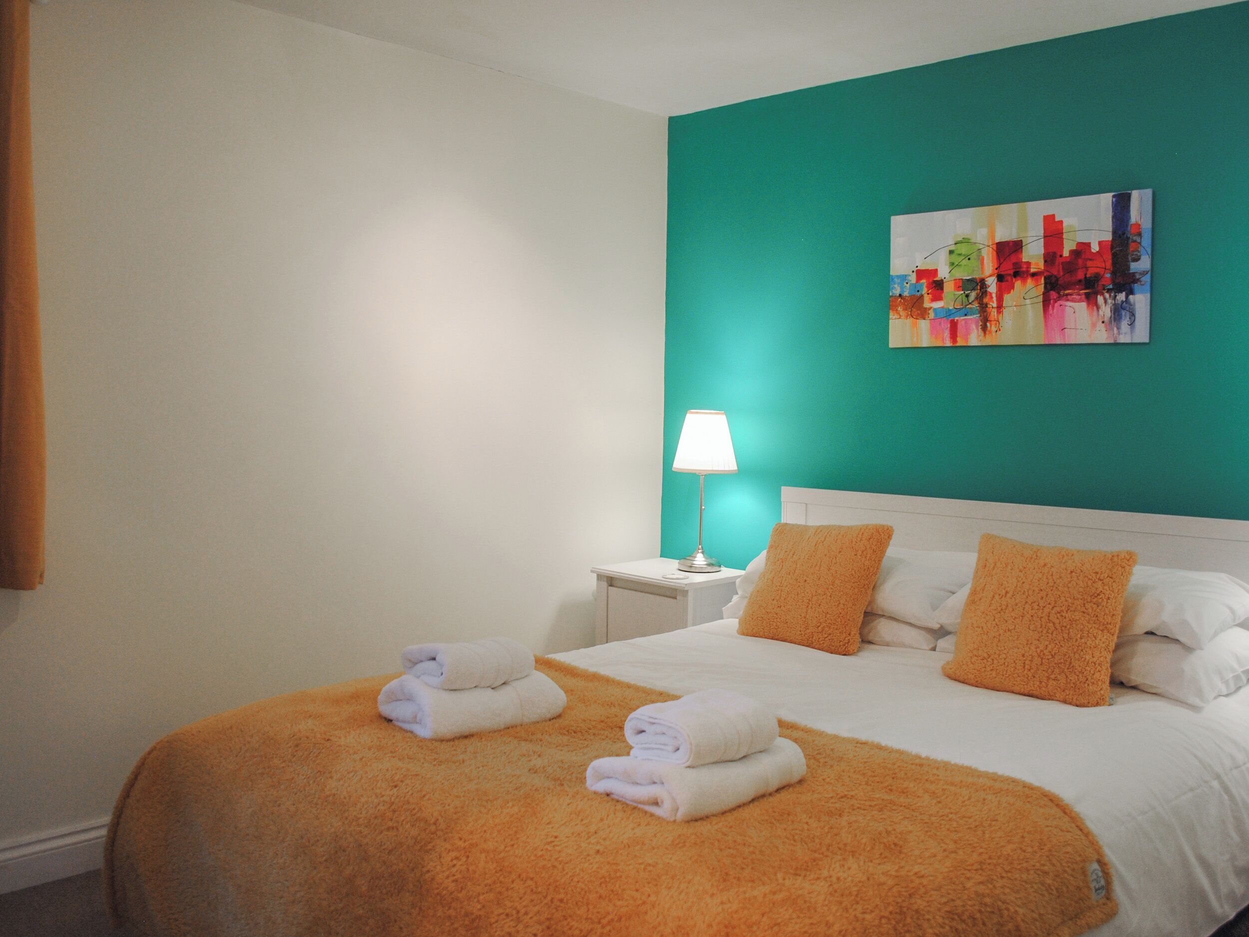 Ein Hotelzimmer mit einem Bett, zwei Kissen, einem Nachttisch mit Lampe und einem Bild an der Wand.
