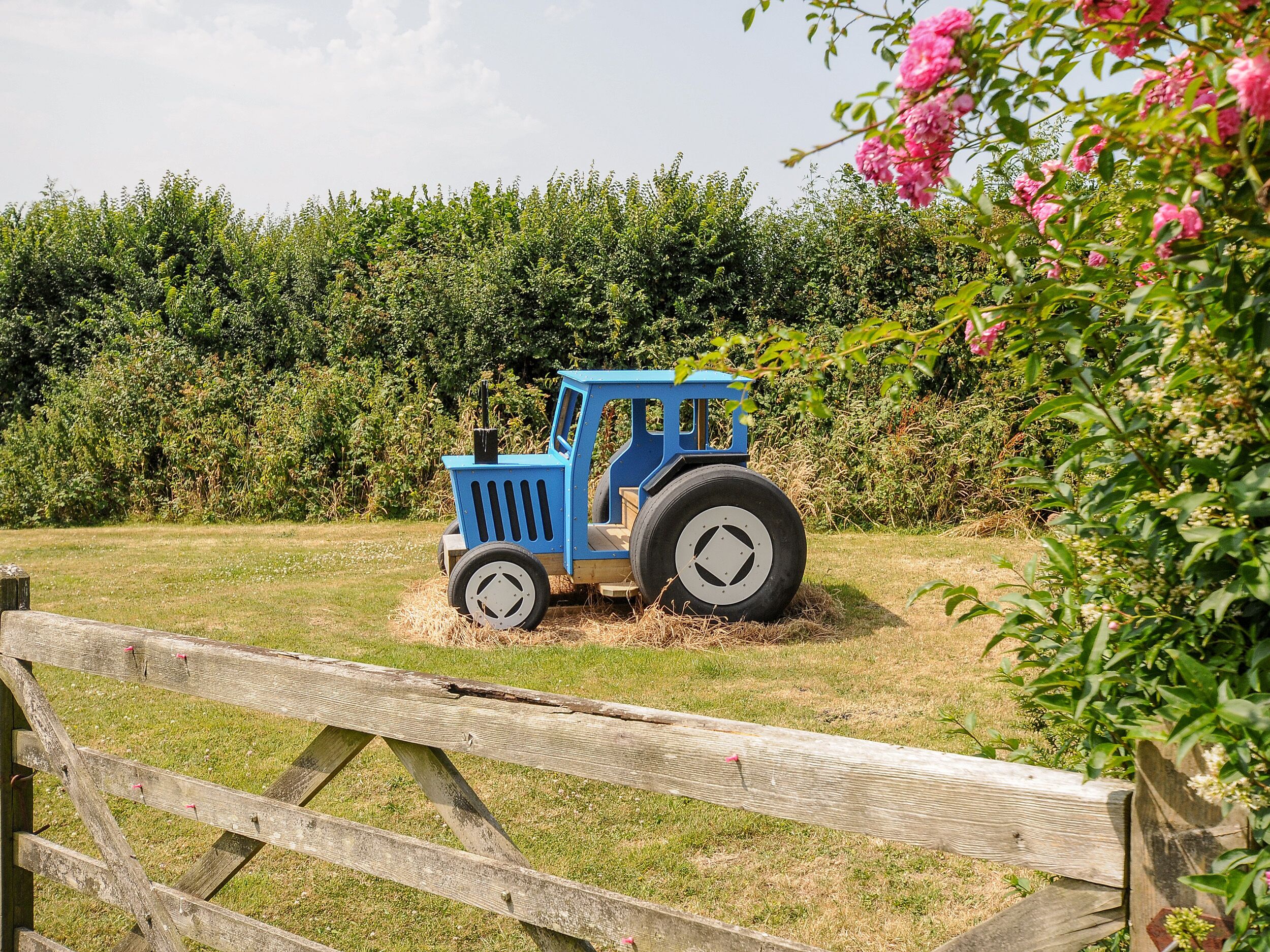 A blue tractor in a grassy field with a wooden fence in the foreground.
