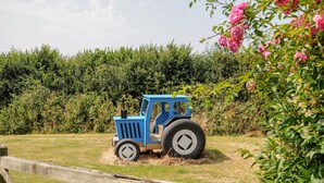 Un tracteur bleu se trouve dans un champ verdoyant, avec une clôture en bois au premier plan.