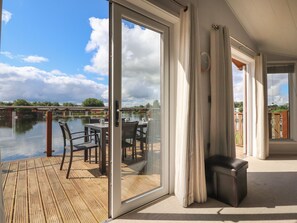 A room with a sliding glass door leading to a wooden deck overlooking a body of water. - Mereside (Carnforth)