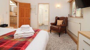 A bedroom with a bed, a chair, a TV, and a view of the bathroom.