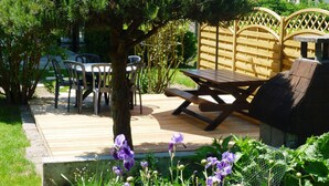 Een houten terras met een picknicktafel en stoelen, omgeven door groen en een kleine tuin.