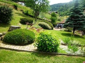 A garden with a paved pathway, neatly trimmed bushes, and a small pond.