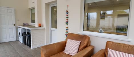Uma sala de estar aconchegante com um sofá de couro marrom, um travesseiro listrado, uma mesinha com um chaleira e uma janela com vista para um edifício.
