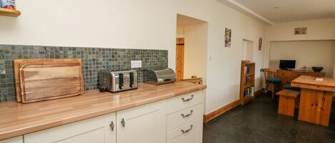 A kitchen with a wooden countertop, two toasters, a cutting board, and a tiled backsplash.