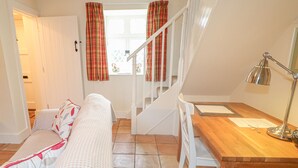 A cozy room with a wooden desk, a white chair, a bed with patterned pillows, and a staircase leading to another level.