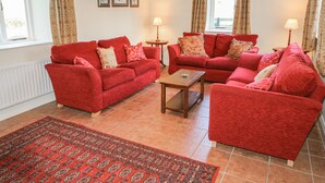 Una sala de estar con dos sofás rojos, una mesa de centro de madera y una alfombra estampada. Hay dos lámparas sobre mesas auxiliares y la habitación tiene una ventana con cortinas.