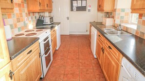 Una cocina con armarios de madera, microondas, horno, lavavajillas y salpicadero de azulejos.