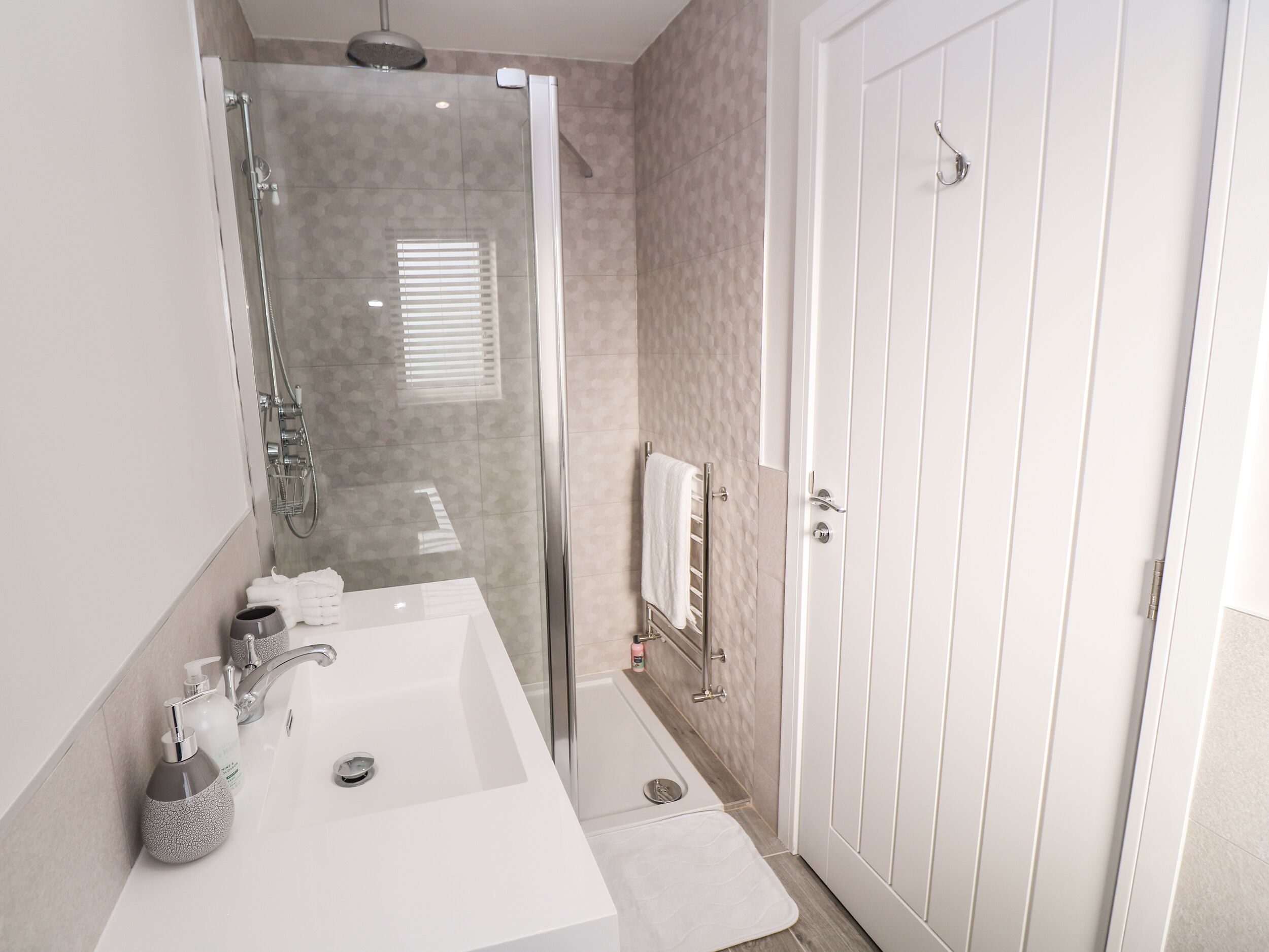 A modern bathroom with a glass-enclosed shower, a white sink with toiletries, and a white door.