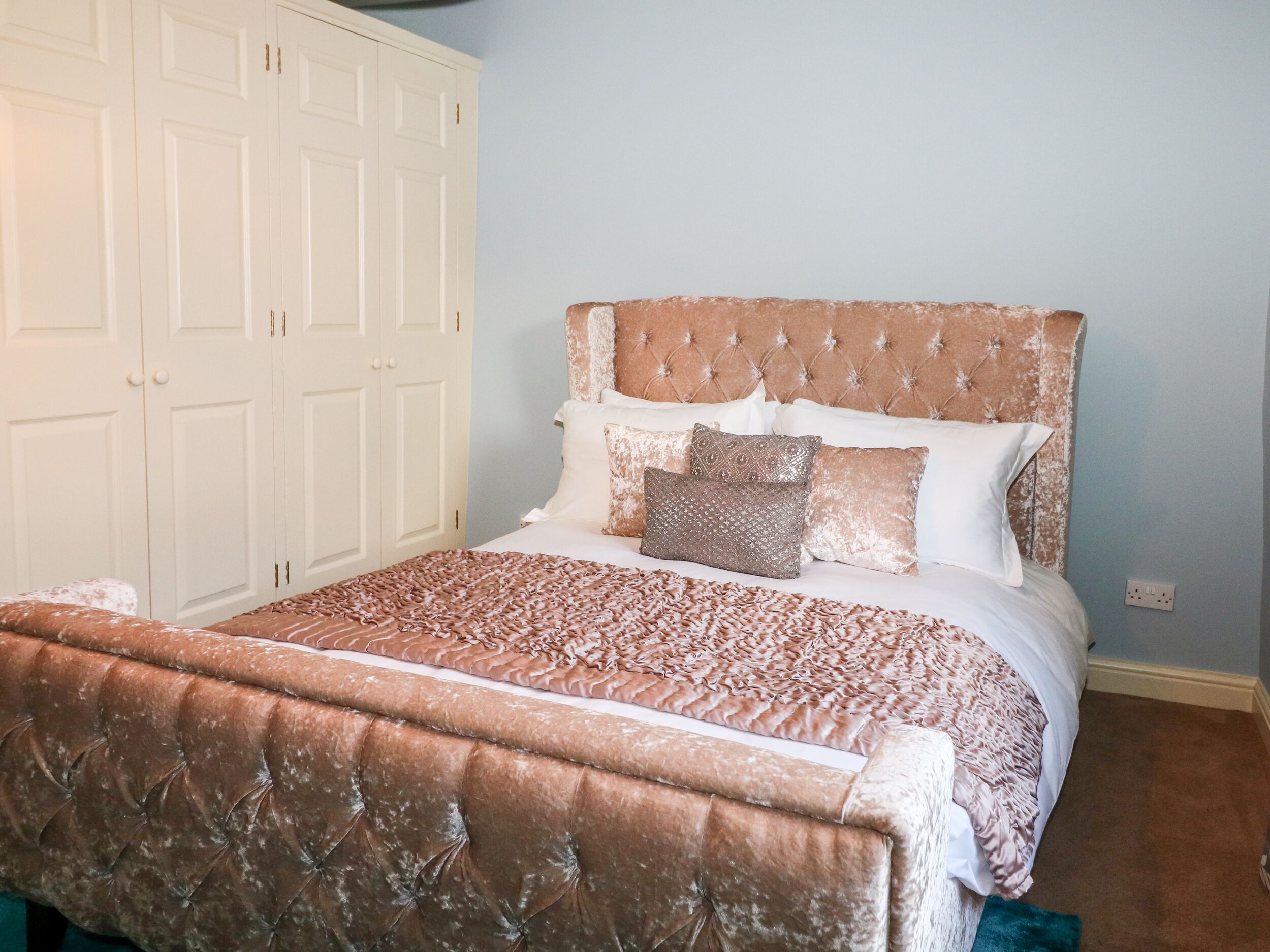 A bedroom with a tufted headboard, a large bed with a patterned bedspread, and white walls.
