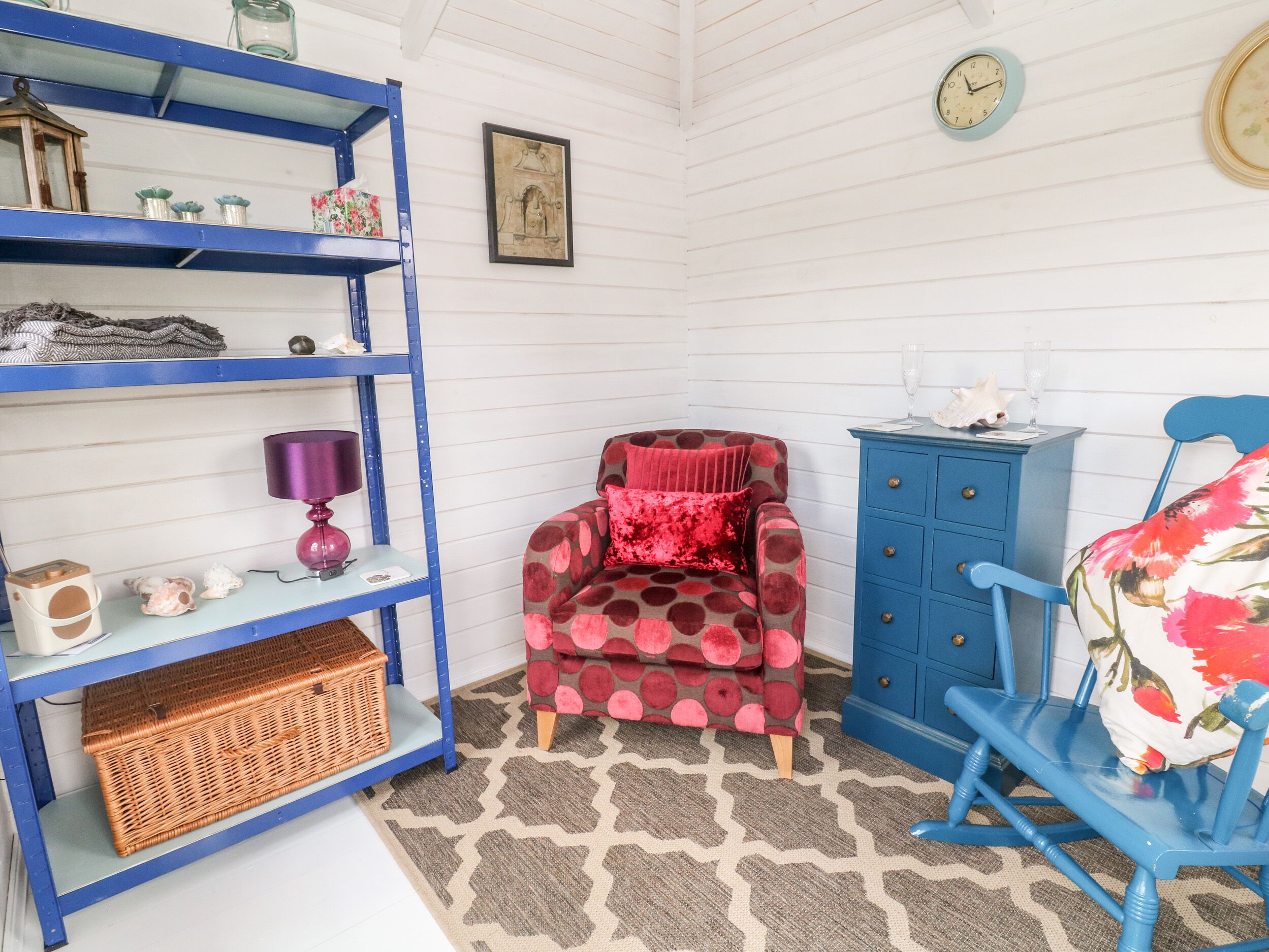 A cozy room with a blue chair, a red armchair, a blue cabinet, and a blue shelving unit.